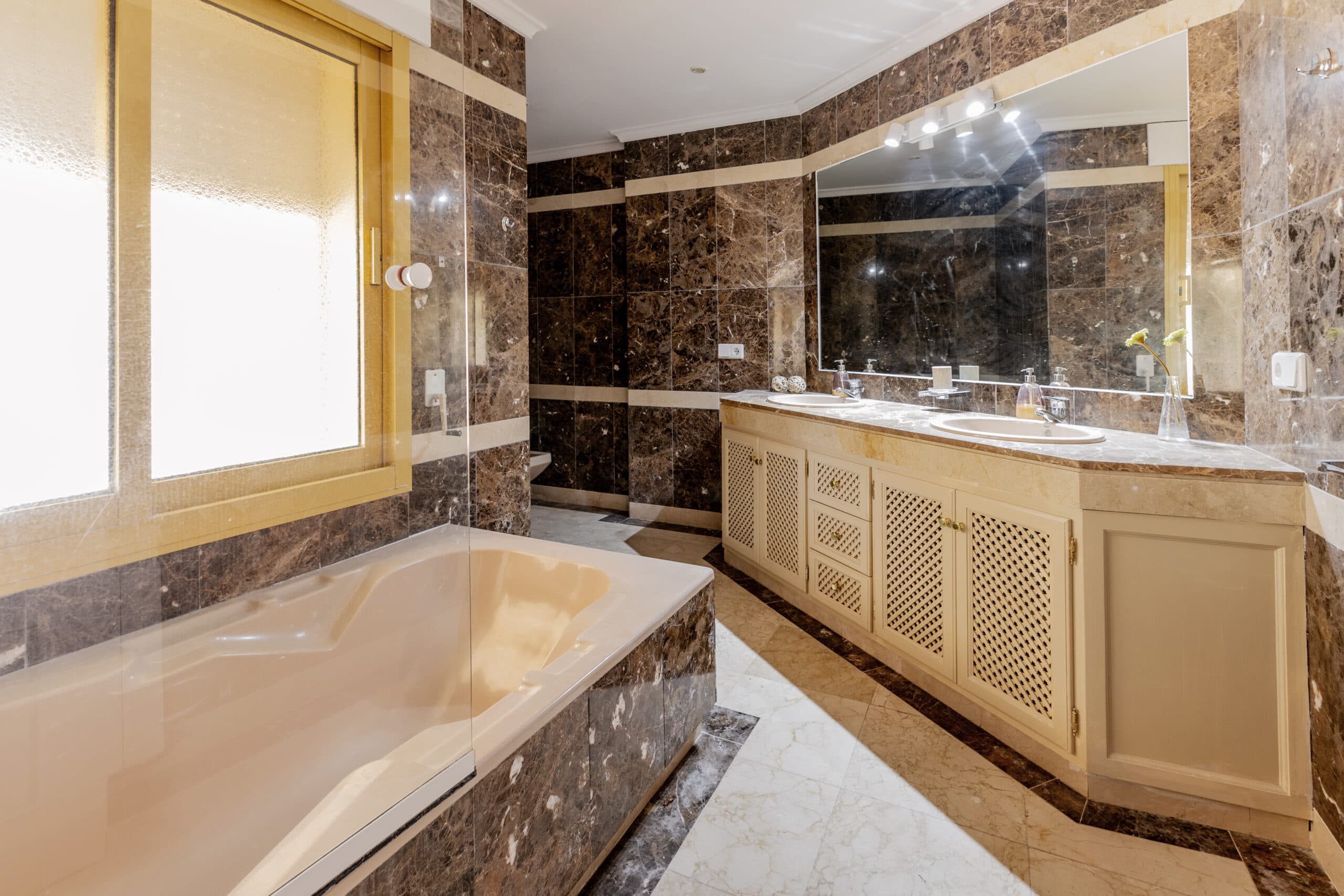 A bathroom in dark marble with a double vanity and a deep bath